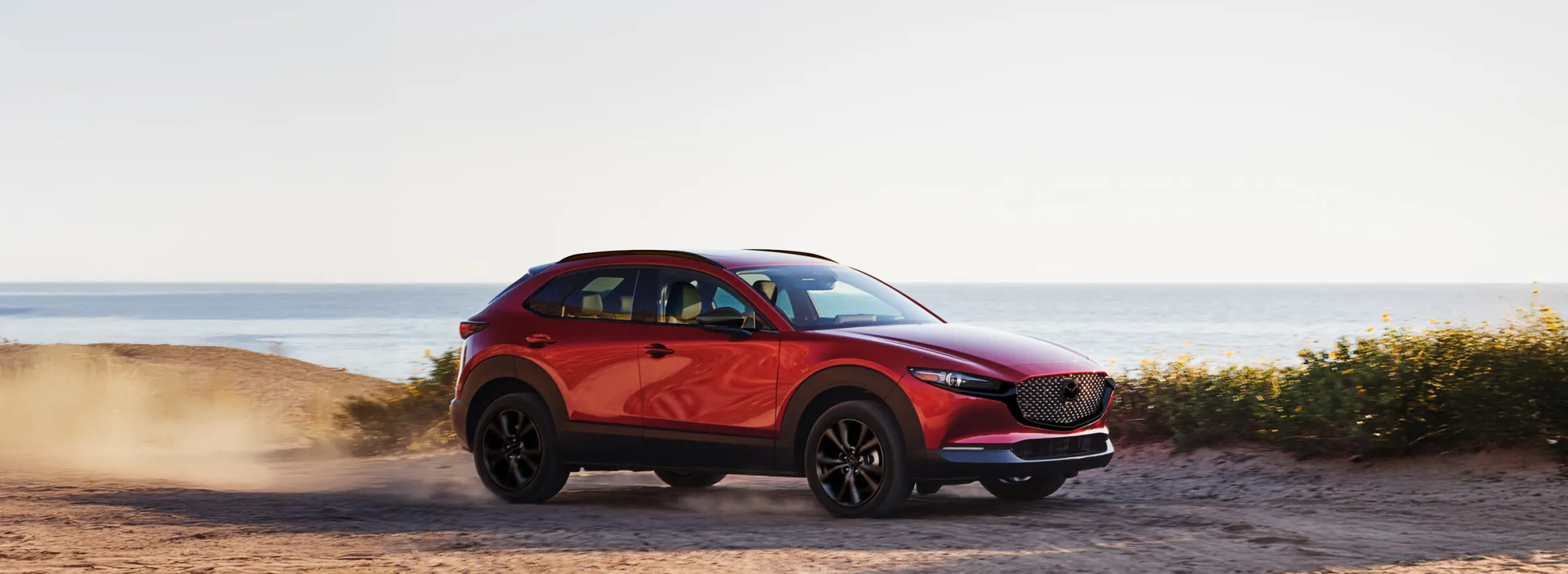 CX-30 rojo sobre un camino de arena junto al mar